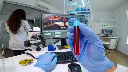 POV of virologist doctor holding tube with blood sampe typing information in pc, analysing patient disease, examining virus evolution. Team of scientists doing research working in equipped laboratory. photo