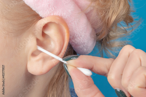 Female cleaning ear with cotton bud on blue background
