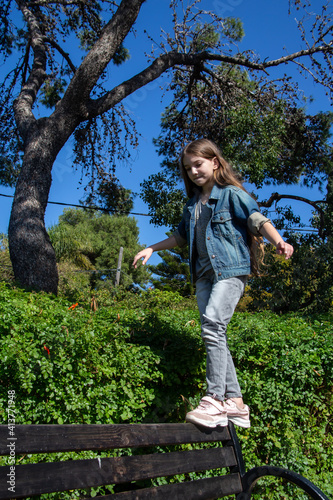 beautiful happy teenage girl walking on the back of a city bench trying to keep her balance outdoors on a sunny day