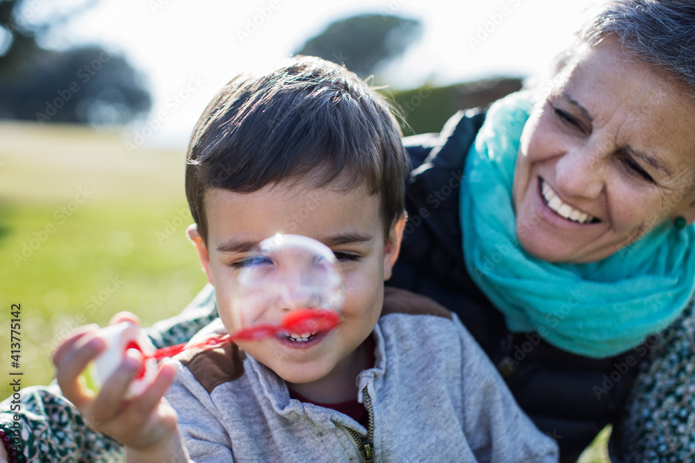 Happy senior woman looking at grandson playing with bubble wand in park Happy senior woman looking at grandson playing with bubble wand in park