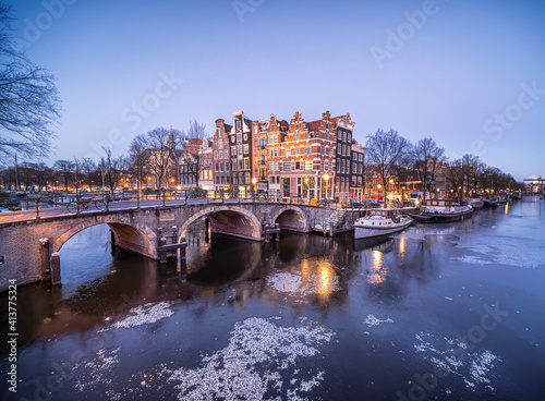 Frozen Amsterdam canals at the Brouwersgracht with famous historic architecture, snow and ice during blue hour with a clear sky