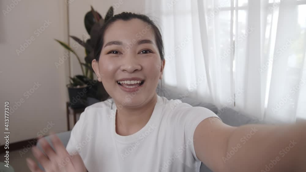 Happy Asian young female sitting on sofa selfie with camera for communication to viewers shooting vlog and video smiling greeting talking having a conversation live streaming at home Happy Asian young female sitting on sofa selfie with camera for communication to viewers shooting vlog and video smiling greeting talking having a conversation live streaming at home