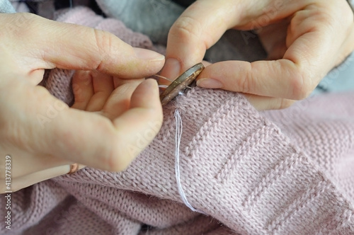 female workers' hands sew a wooden button to a jacket. close-up.