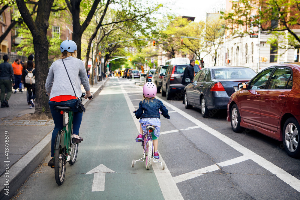 Rear view of mother and daughter riding bicycles in city Rear view of mother and daughter riding bicycles in city