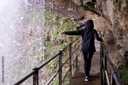 Rear view of woman touching Trummelbach Falls while walking on footbridge under rock photo