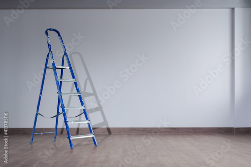 Obraz na plátně A dirty blue metal stepladder against a newly painted gray wall in a new building