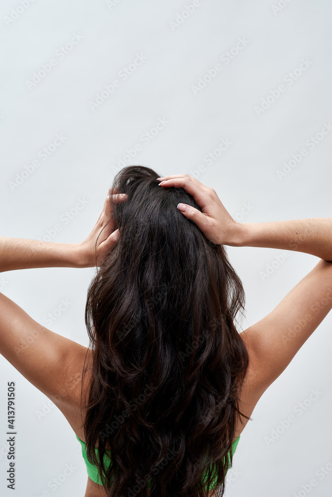 Naklejka premium Rear view of young woman wearing green underwear posing against light background, showing off her healthy long dark brown hair