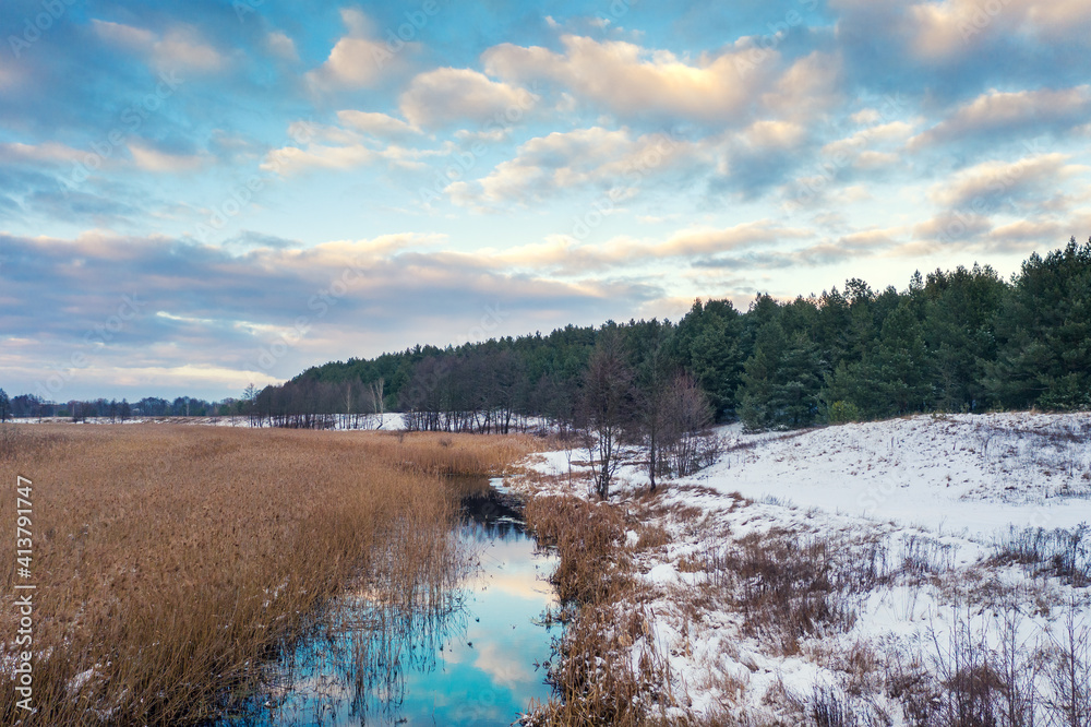 View of a winding reeded stream in the evening. Beautiful natural landscape with a cloudy evening sky