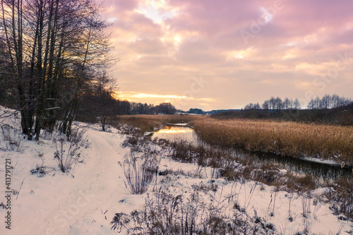 Rural landscape in winter. View of a brook and cloudy sky at sunset
