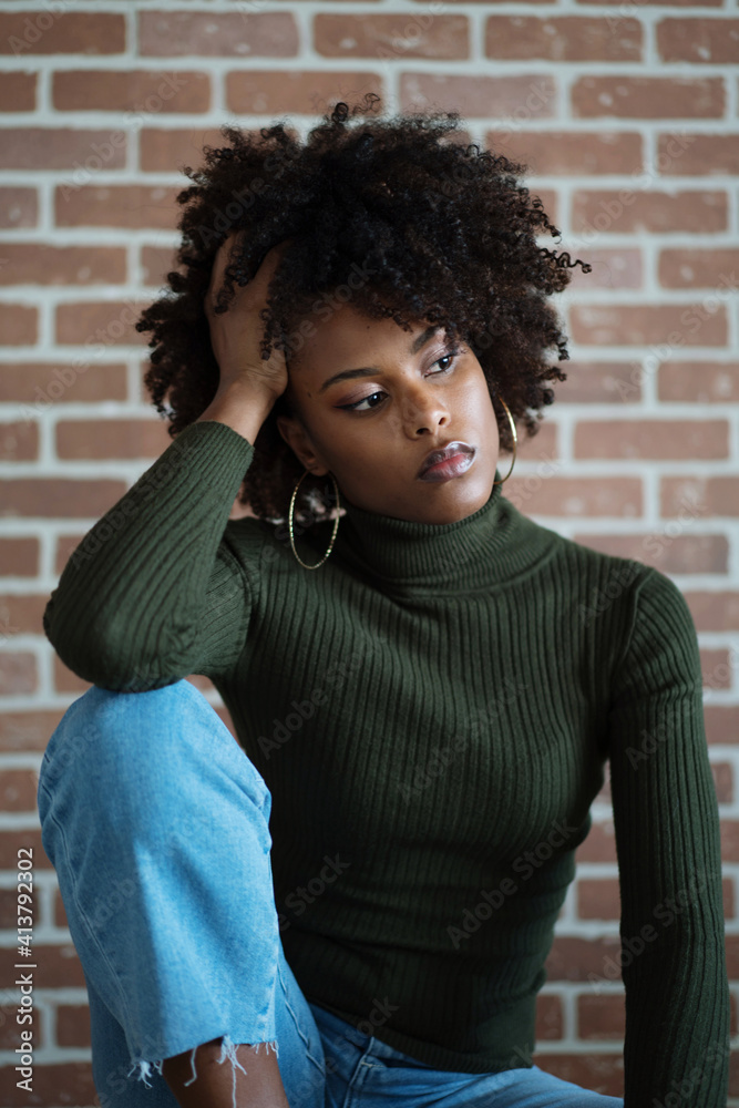 Beautiful black woman with afro hair sitting on the chair against the brick wall background Beautiful black woman with afro hair sitting on the chair against the brick wall background