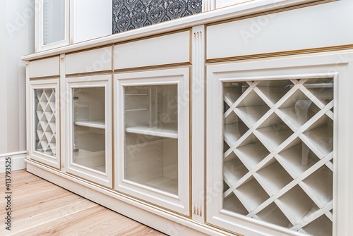 Classical style white showcase with glass doors and gilding on the background of black and white wallpaper with floral pattern