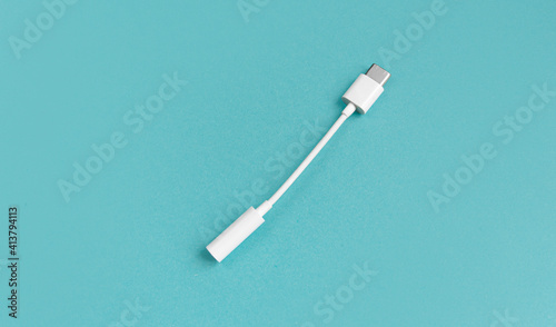 An adapter for a USB to 3.5mm type c headphone cable on a smartphone. white cable and 3.5 audio cable for phone on android mm on a blue background. View from above. copy space.