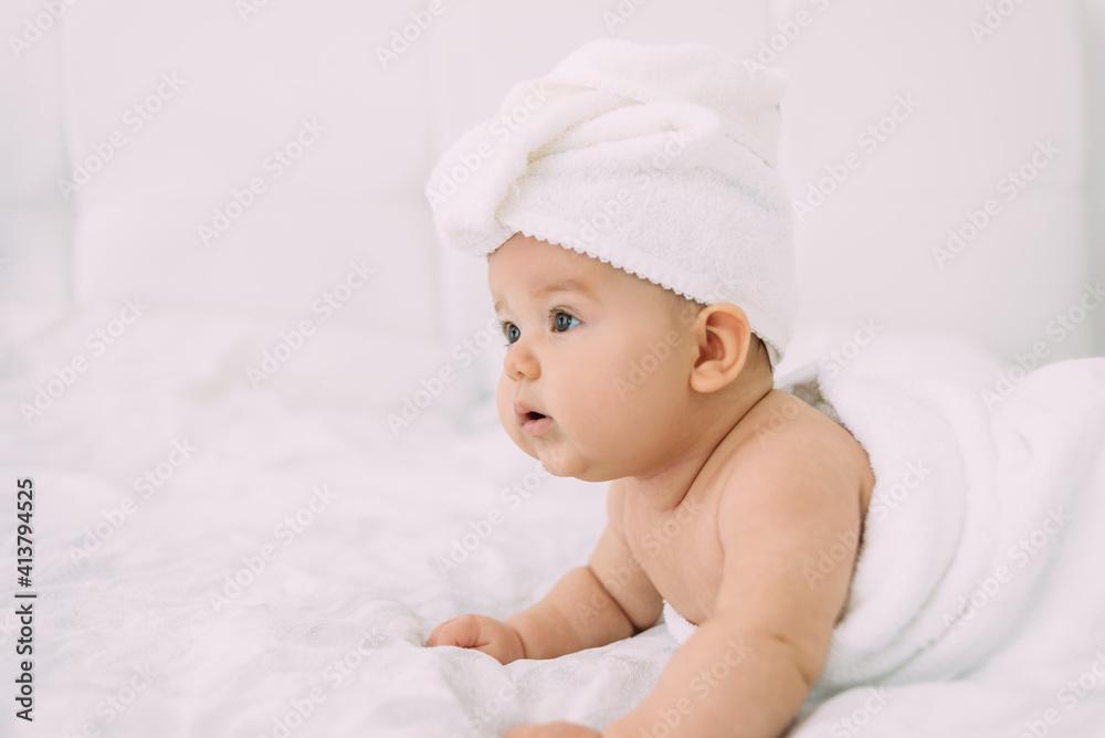 The girl lies on a white bed with a towel on her head and body. Hygiene and baby care concept. The girl lies on a white bed with a towel on her head and body. Hygiene and baby care concept.