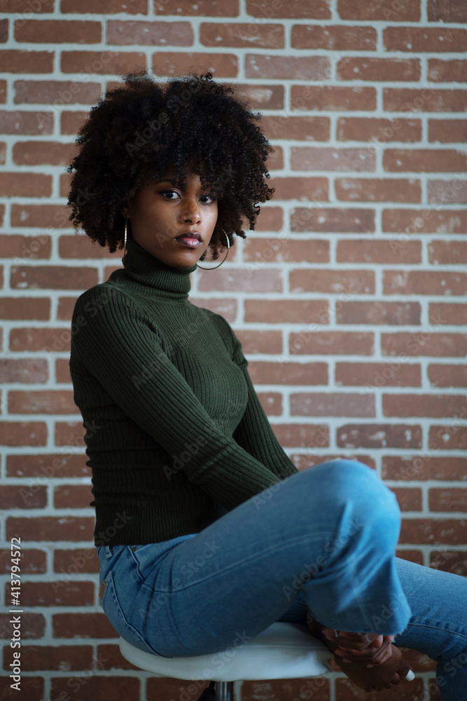 Beautiful black woman with afro hair sitting on the chair against the brick wall background Beautiful black woman with afro hair sitting on the chair against the brick wall background