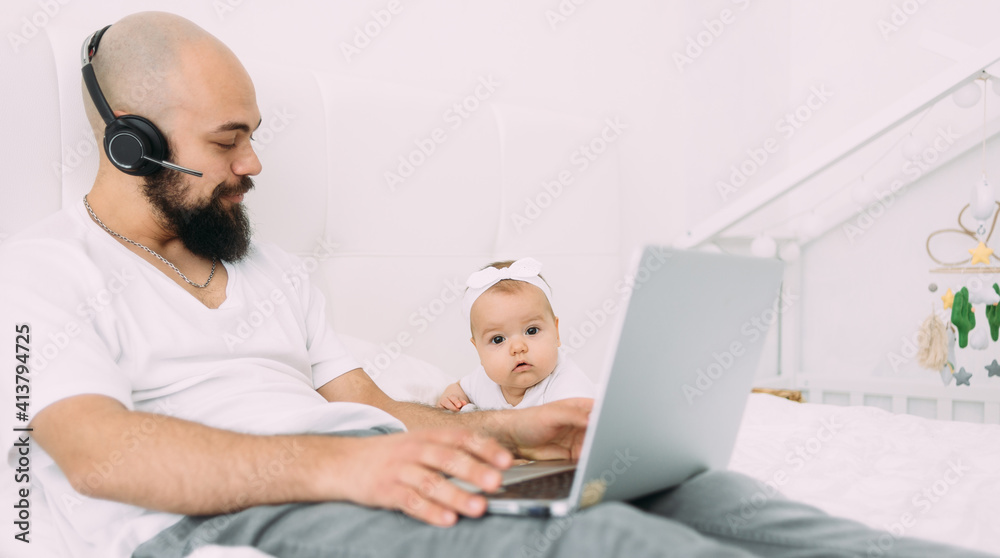 Obraz premium A young dad is sitting on a bed with a child together at home at a computer. A father works on a laptop.