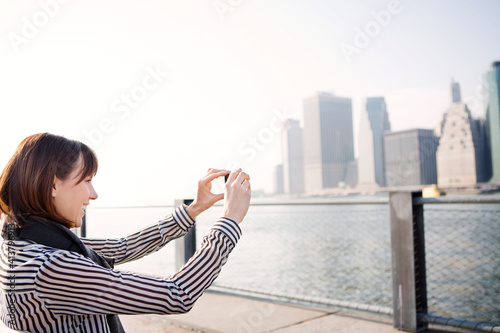 Happy woman photographing cityscape by East River photo