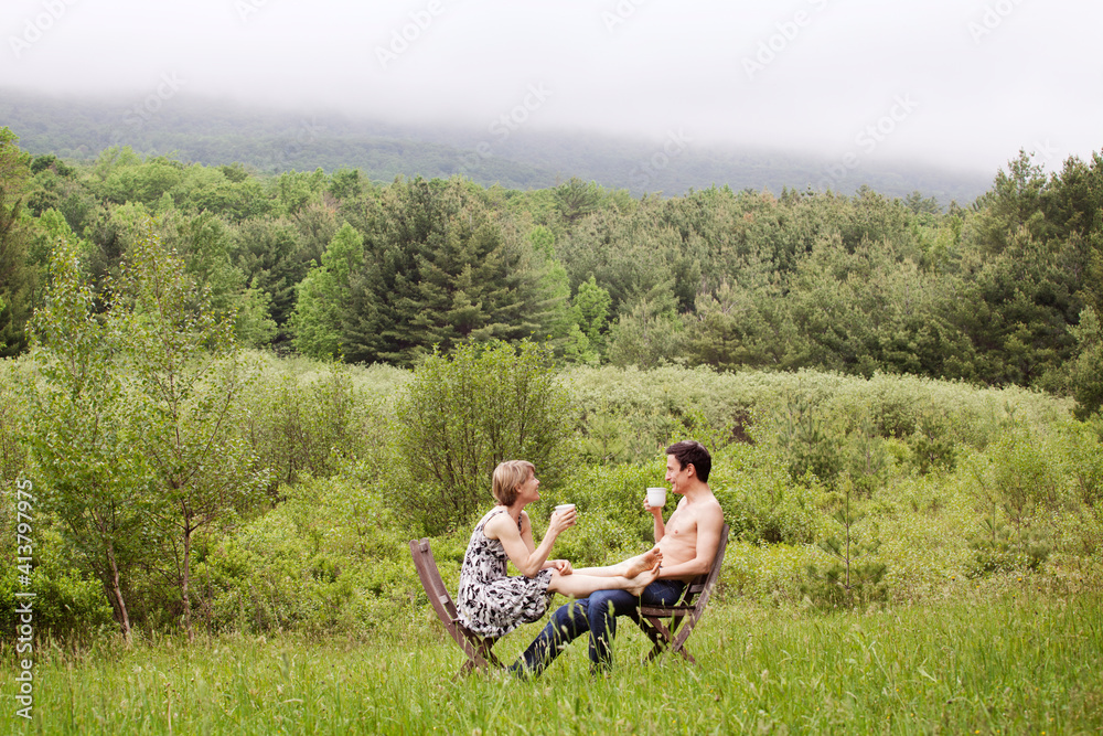 Couple enjoying coffee while sitting on chair in field Couple enjoying coffee while sitting on chair in field