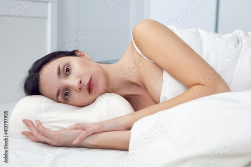 woman in a white t-shirt is lying on the bed and a pillow is under the blanket in the room