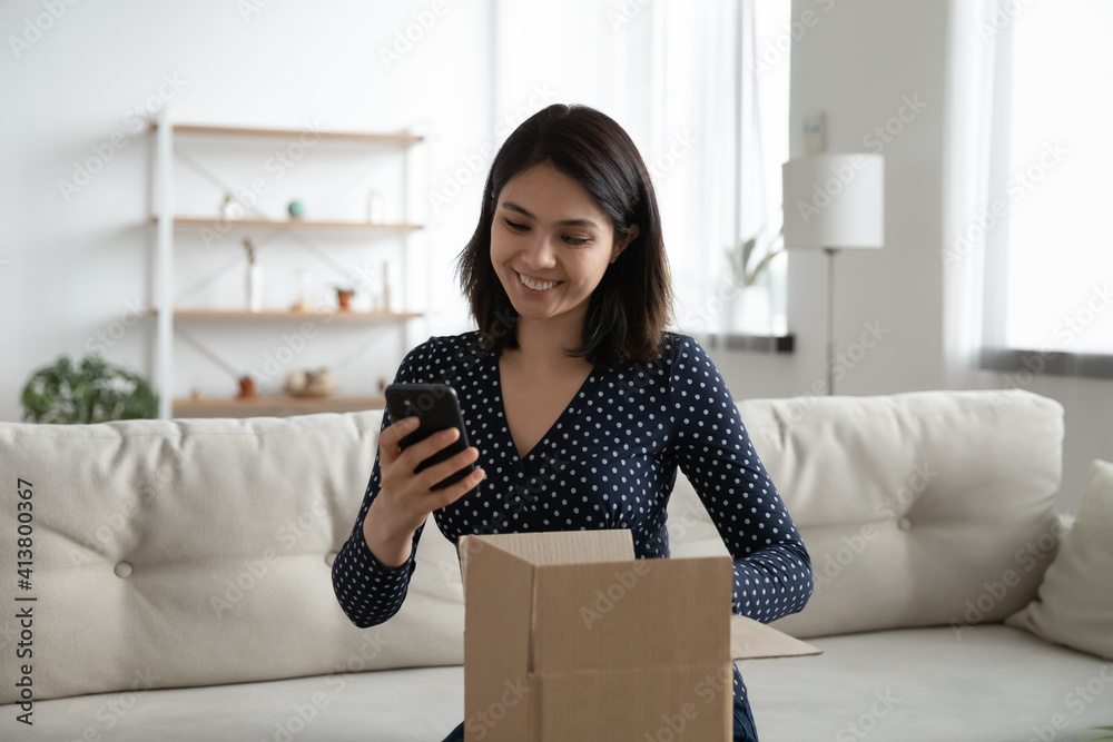 Smiling woman satisfied client hold opened cardboard box parcel text positive feedback to shop website. Grateful young asian female call friend on phone to thank for birthday surprise received by mail Smiling woman satisfied client hold opened cardboard box parcel text positive feedback to shop website. Grateful young asian female call friend on phone to thank for birthday surprise received by mail
