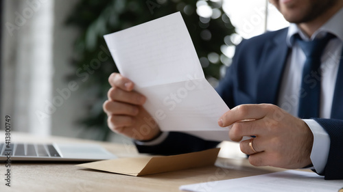 Crop close up businessman sit at desk reading post paper letter or correspondence in office. Male employee or director receive consider postal paperwork or mail notification at workplace. photo