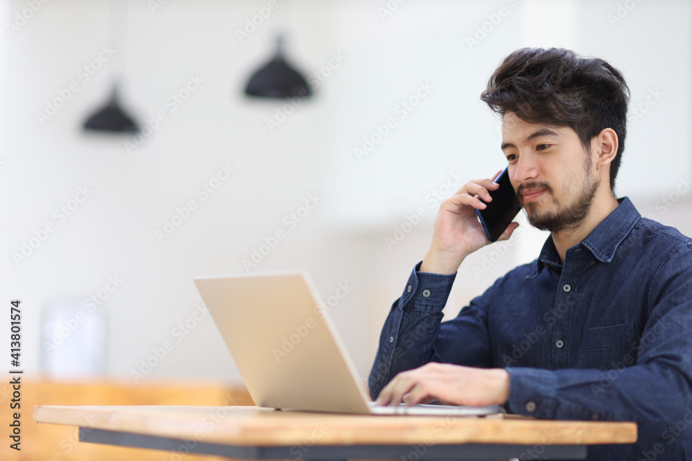 young businessman asia working on laptop and talking mobile phone in cafe. Asian man calling mobile phone and looking documents on computer.