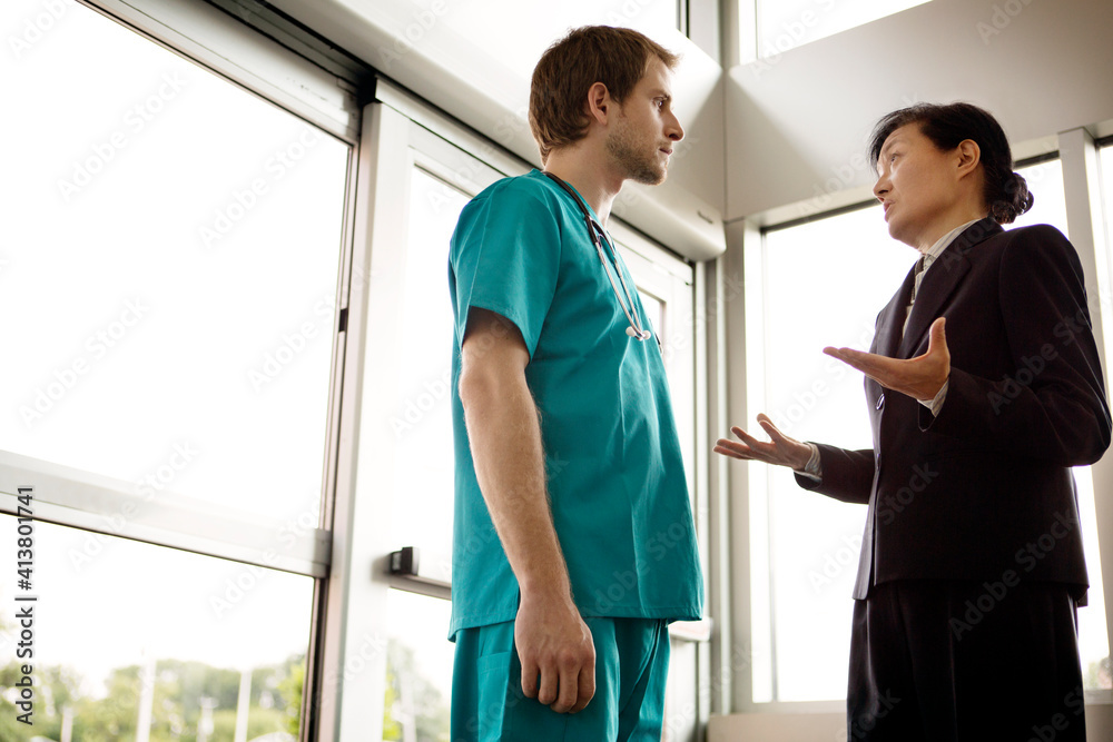 Low angle view of doctor talking with businesswoman while standing in hospital