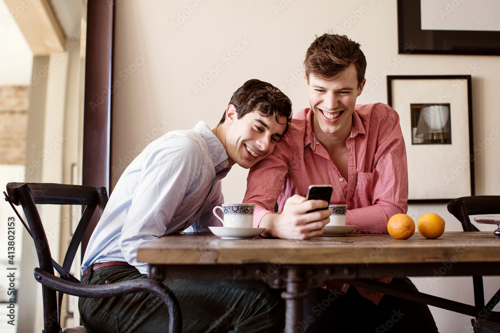 Smiling gay men looking at smart phone while sitting by table Smiling gay men looking at smart phone while sitting by table