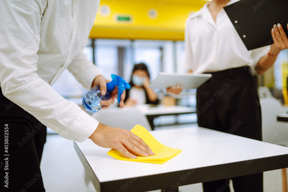 Cleaning and disinfection of the desktop. Man in protective sterile mask cleans the working desk with the wiping cloth and antibacterial sprayer. Covid-2019. Cleaning and disinfection of the desktop. Man in protective sterile mask cleans the working desk with the wiping cloth and antibacterial sprayer. Covid-2019.