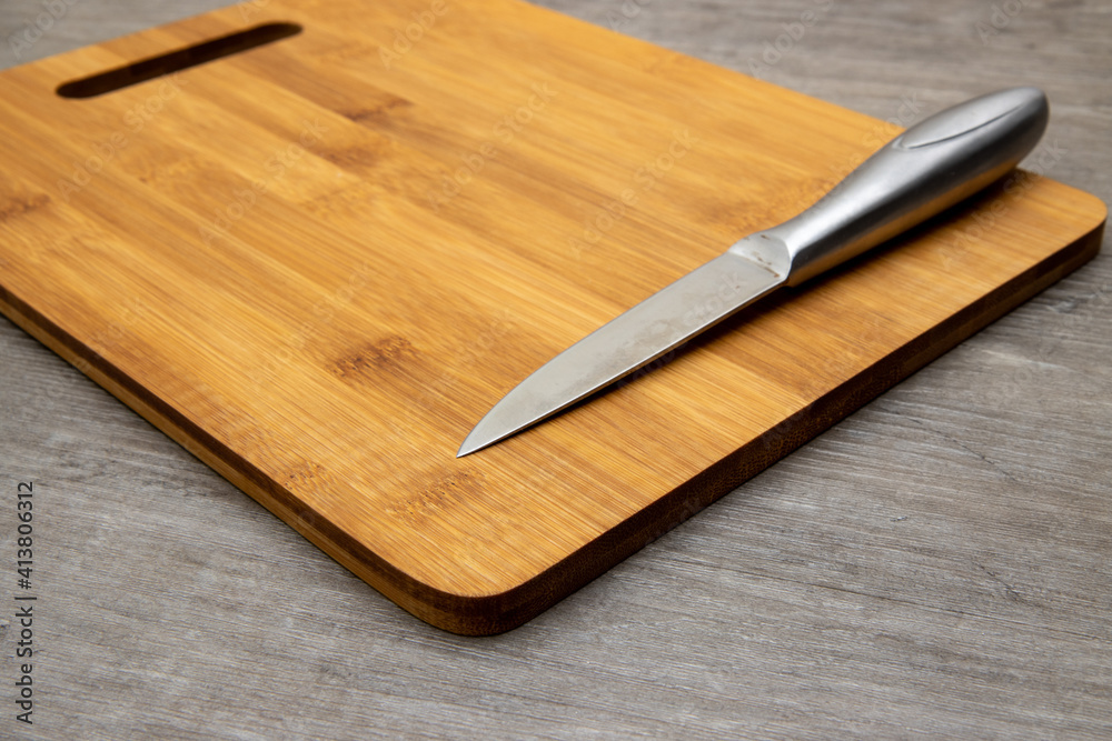 A wooden chopping board in a kitchen with a silver metal knife A wooden chopping board in a kitchen with a silver metal knife