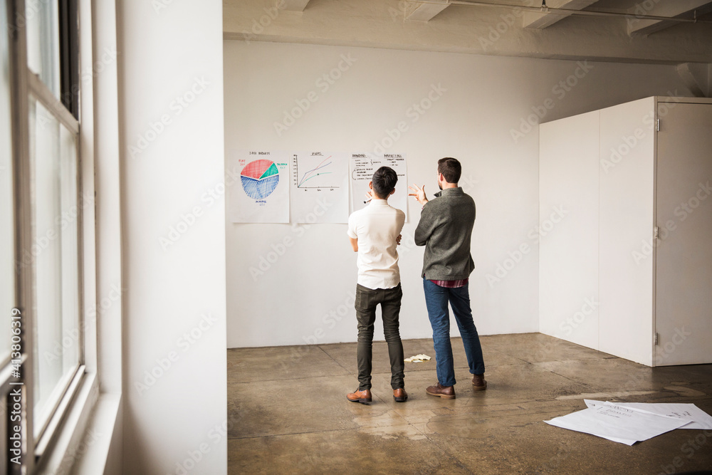 Rear view of business colleagues looking at charts while standing in creative office