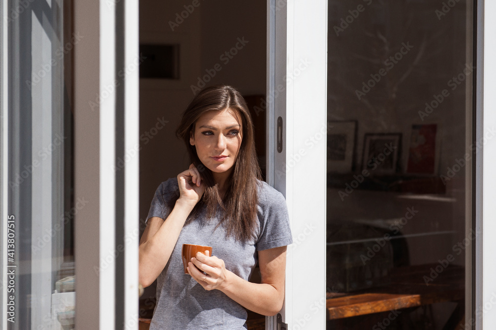 Beautiful woman holding coffee cup and standing at window Beautiful woman holding coffee cup and standing at window