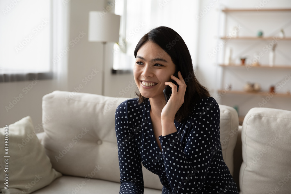 Confident young asian lady spend time in pleasant phone conversation on sofa at living room. Smiling vietnamese female hold cell to ear communicate with relatives abroad by international roaming call Confident young asian lady spend time in pleasant phone conversation on sofa at living room. Smiling vietnamese female hold cell to ear communicate with relatives abroad by international roaming call