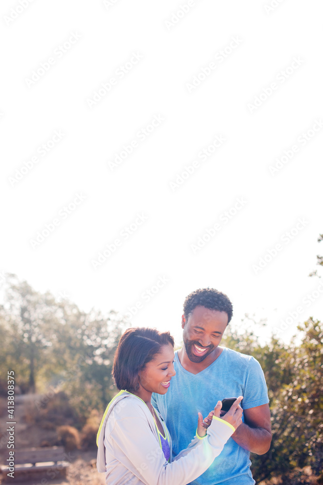 Happy couple using phone while standing on field against clear sky Happy couple using phone while standing on field against clear sky