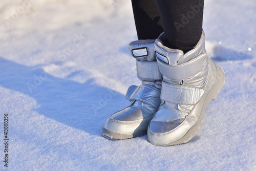Children's winter boots in silver color on the snow