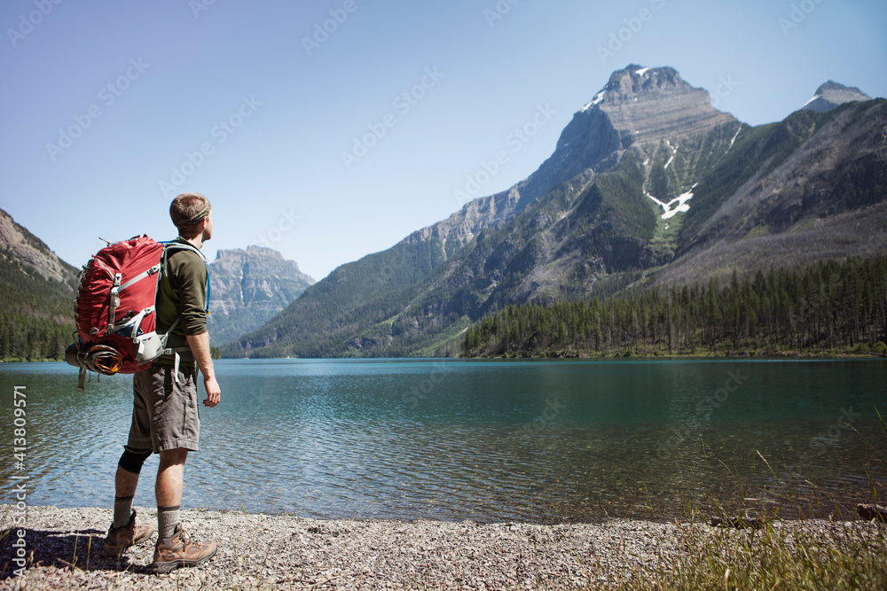 Hiker carrying backpack while standing by lake at Glacier National Park