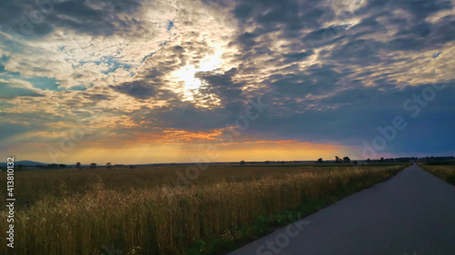 Cloudy sky over the grain field with the rays of the sun breaking through.