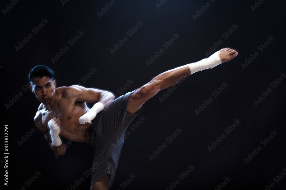 Determined male kickboxer kicking against black background Determined male kickboxer kicking against black background