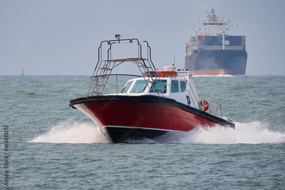 Naklejka premium Schnell fahrendes Lotsenboot mit Container Schiff im Hintergrund
