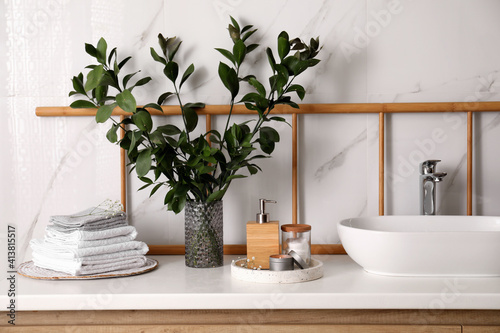 Vase with green branches  towels and soap dispenser on countertop in bathroom