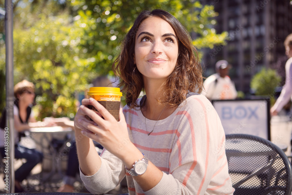 Thoughtful woman holding disposable coffee cup at sidewalk cafe Thoughtful woman holding disposable coffee cup at sidewalk cafe