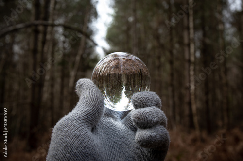 Lens Ball held by gloved hand in English forest on a grey day. Lensball optics dark dramatic outdoors