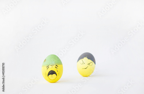 Two yellow eggs on a white isolated background. Eggs in hats with funny sad and cheerful faces. Celebration and joy. Happy easter. Hand-painted eggs. Easter garland.