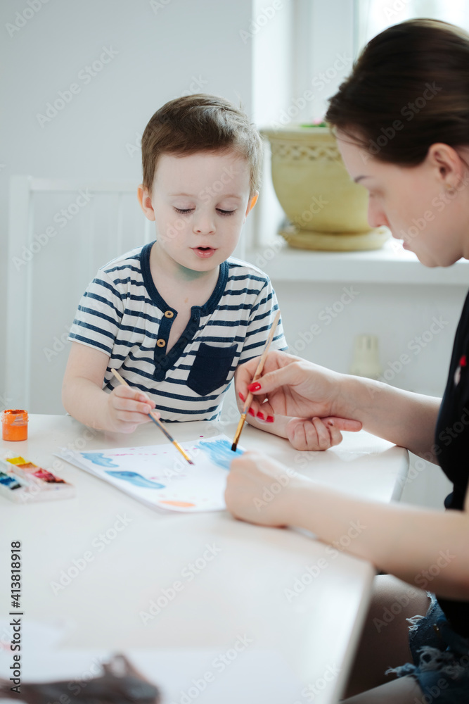 mom with a child in quarantine draws colorful paints at a white table mom with a child in quarantine draws colorful paints at a white table