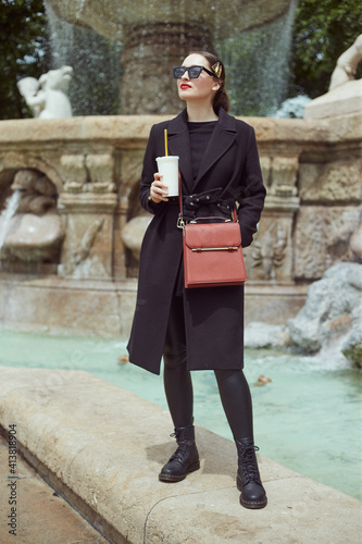 Fashion portrait of young woman standing on the wall by the fountain photo