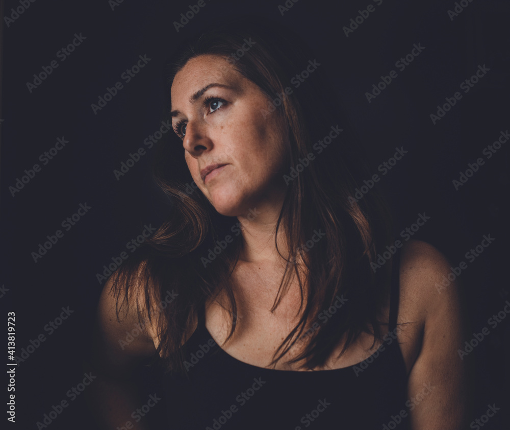 Thoughtful woman standing in darkroom at home Thoughtful woman standing in darkroom at home