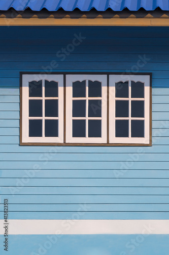 Sunlight on surface of 3 white windows on blue wooden wall of the old vintage house in vertical frame