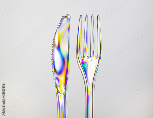 Fotografie Transparent plastic fork and knife, rainbow colored by photoelasticity isolated on light gray background