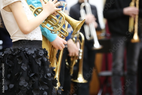 A little delicate girl in a white blouse and a black full skirt plays a musical instrument on an old worn trumpet in a jazz band among adult musicians. The concept of education and training photo