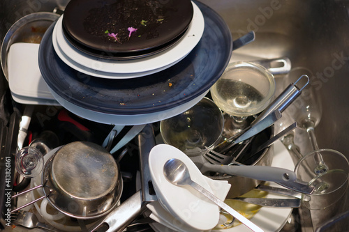 Close-up full frame view of a kitchen sink full of dirty plates, glasses, flatware, and utensils after an extensive dinner for two
