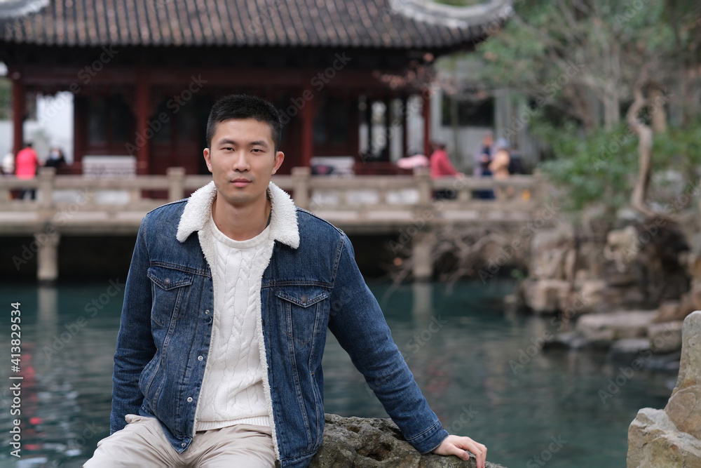 one Asian young man sitting in traditional Chinese garden, looking at camera